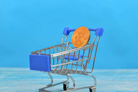 Bitcoin coin in a consumer shopping cart on a blue background.