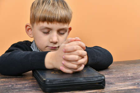 A child prays on his knees with his hands on the Bible.の写真素材