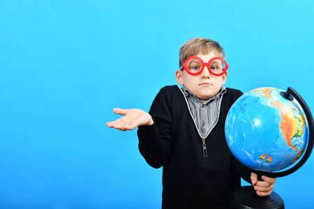 A boy in funny glasses holds a globe in his hand and looks for cities on it.の写真素材