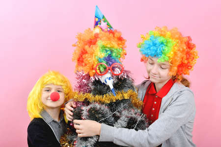 Boy and girl in clown wig hugs funny new year christmas tree in wig.