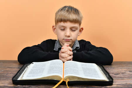 The boy bowed his knees in prayer before the open Bible.の写真素材