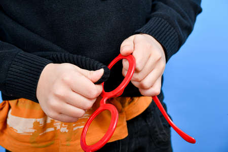 The boy wipes his red glasses in which there are no glasses, stupid boy.