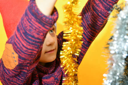 A joyful boy wearing a Santa Claus hat decorates the Christmas tree with New Year's toys and...