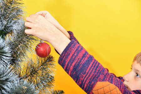 The boy decorates the Christmas tree with New Year's toys and glittering tinsel.の写真素材