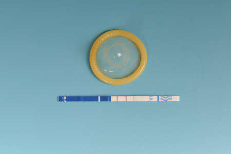 Condom and positive pregnancy test on a blue background.の写真素材