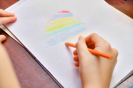 The girl draws a heart on a white sheet of paper and paints it in the form of a rainbow with colored...