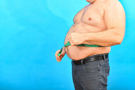 A man in jeans measures a large fat waist with a green centimeter.の写真素材