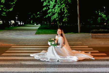 A bride in a white dress sits on the pavement at a pedestrian crossing on the roadway.の写真素材