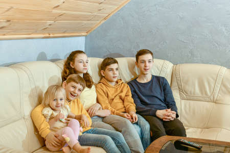 Five children sit on a leather sofa and watch TV.