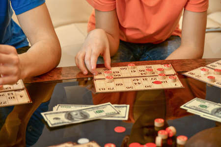 Lotto cards, chips and money lie on a glass coffee table. People play lotto for money.