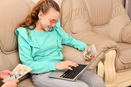 A young girl with a laptop in the office accepts cash dollars from customers and fills in the data...