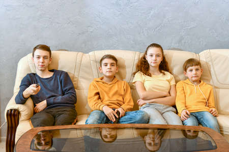 The boy switches TV channels with a remote control. Four children are watching TV.の写真素材