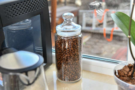 Glass jar with coffee beans next to the coffee machine in the kitchen.