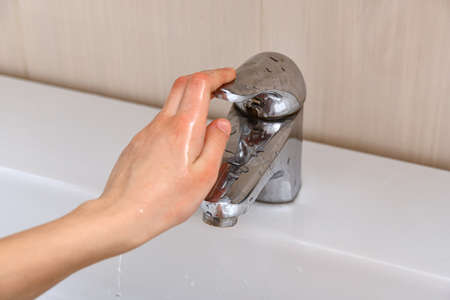 The girl closes the tap with water after washing her hands.