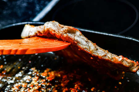 Fried pork steaks in a frying pan. The cook turns the meat for frying.