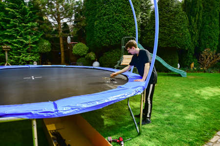 A boy builds a new trampoline at home and stretches the trampoline fabric with springs.の写真素材