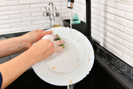A woman washes dishes in the kitchen with tap water.の写真素材