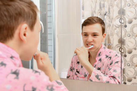 The guy in the bathroom brushes his teeth with a toothbrush in front of the mirror.の写真素材