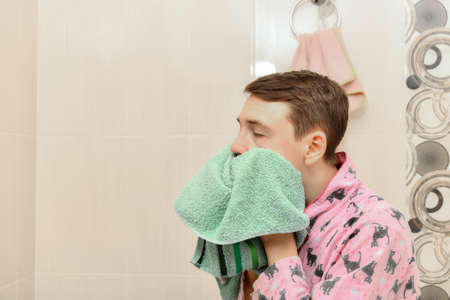 A young man wipes his face with a towel in the bathroom.の写真素材