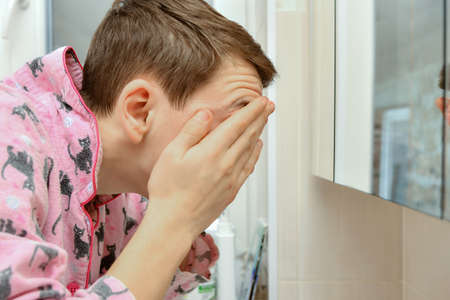 A young man washes his face with water from the tap in the washbasin and wipes his face with his hands in the bathroom.の写真素材