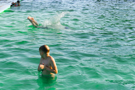 A boy in the pool watches his friend jump into the water.