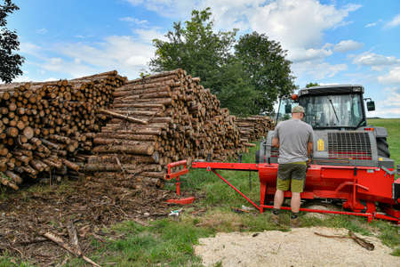 A worker at a sawmill operates a hydraulic plant for chopping and sawing logs for firewood.の写真素材