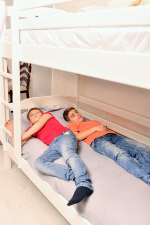 Two adult boys sleep dressed on the bed.