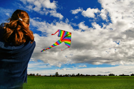 The girl controls a kite flying among the blue cloudy sky.の写真素材