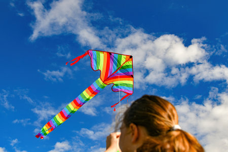 The girl controls a kite flying among the blue cloudy sky.の写真素材