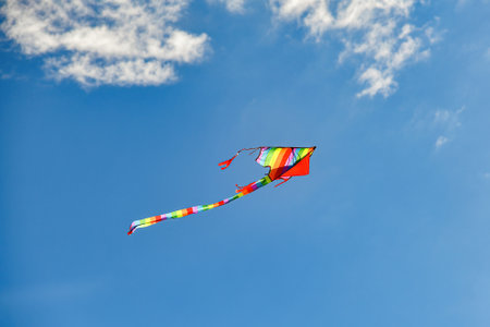 A colorful kite soars among the blue cloudy sky.の写真素材