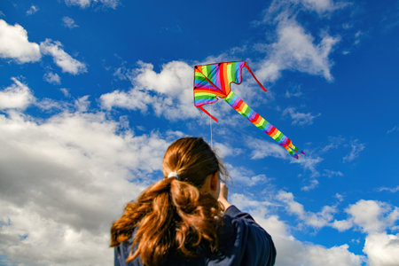 A girl launches a colored kite into the blue cloudy sky.