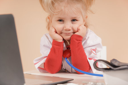 A little girl dressed as a doctor sits near a laptop.の写真素材