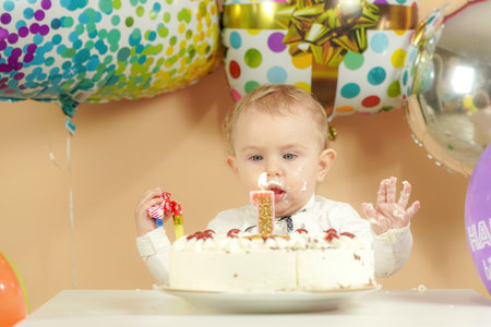 Surprised birthday girl on the background of balloons looks at a burning candle.の写真素材