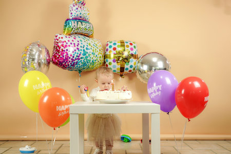 A small child for a birthday near a birthday cake on the background of balloons.の写真素材