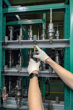 To operate a CNC machine, a worker selects and inspects the required cutter from the rack and tool...
