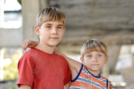 Two brothers are standing in an embrace against the backdrop of an unfinished and abandoned...