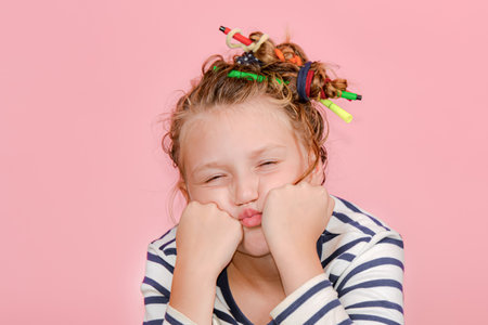A girl with a funny hairstyle in a striped T-shirt touches her hair, is surprised and makes funny...