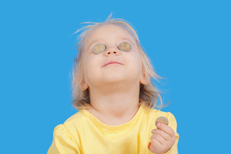Joyful little girl holding money coins near her eyes.の写真素材