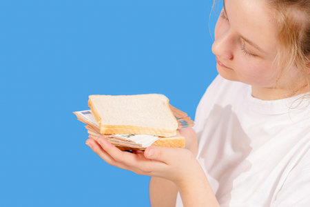 The girl is holding a piece of bread in her hands and euro banknotes on top.の写真素材