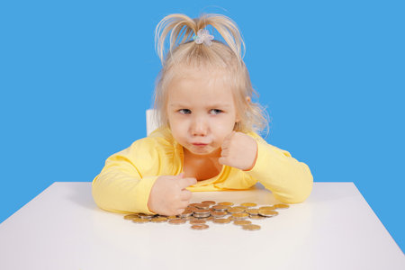 The girl covers the coins with her hands, which are lying on the table. The child does not want to give the money.の写真素材
