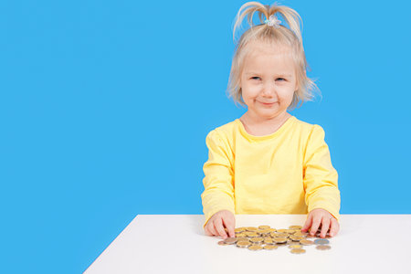 A girl collects and counts coins scattered on the table.の写真素材