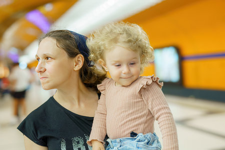 A mother with a little daughter in her arms is waiting for an electric train in an underground metro station.の写真素材