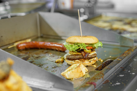 A cook in a restaurant prepares a bacon burger and cutlets with salad and cheese.の写真素材