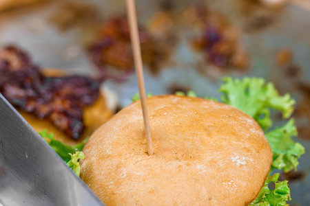 A cook in a restaurant prepares a bacon burger and cutlets with salad and cheese.の写真素材