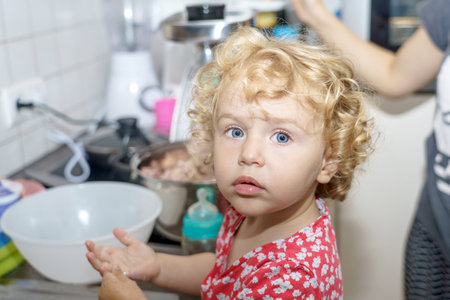 A little girl helps her mother in the kitchen with cooking.の写真素材