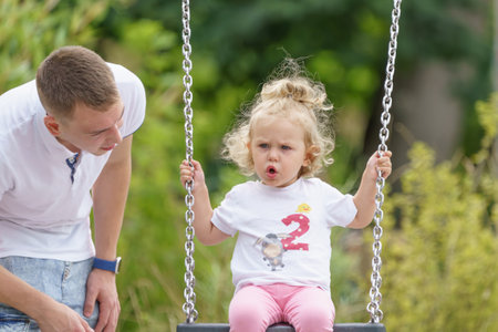 A young father pushes his little daughter on a swing in the park.の写真素材