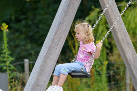 A little girl is riding on a chain swing in a park.の写真素材