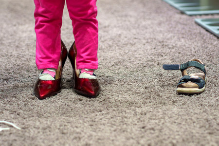 Little girl looking at adult women's red shoes in a store.の写真素材