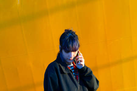 Alternative girl in yellow background talking smart phoneの写真素材