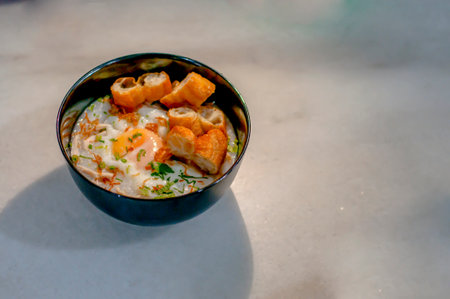 chicken porridge with half boiled egg and fried bread slices on ceramic tableの写真素材